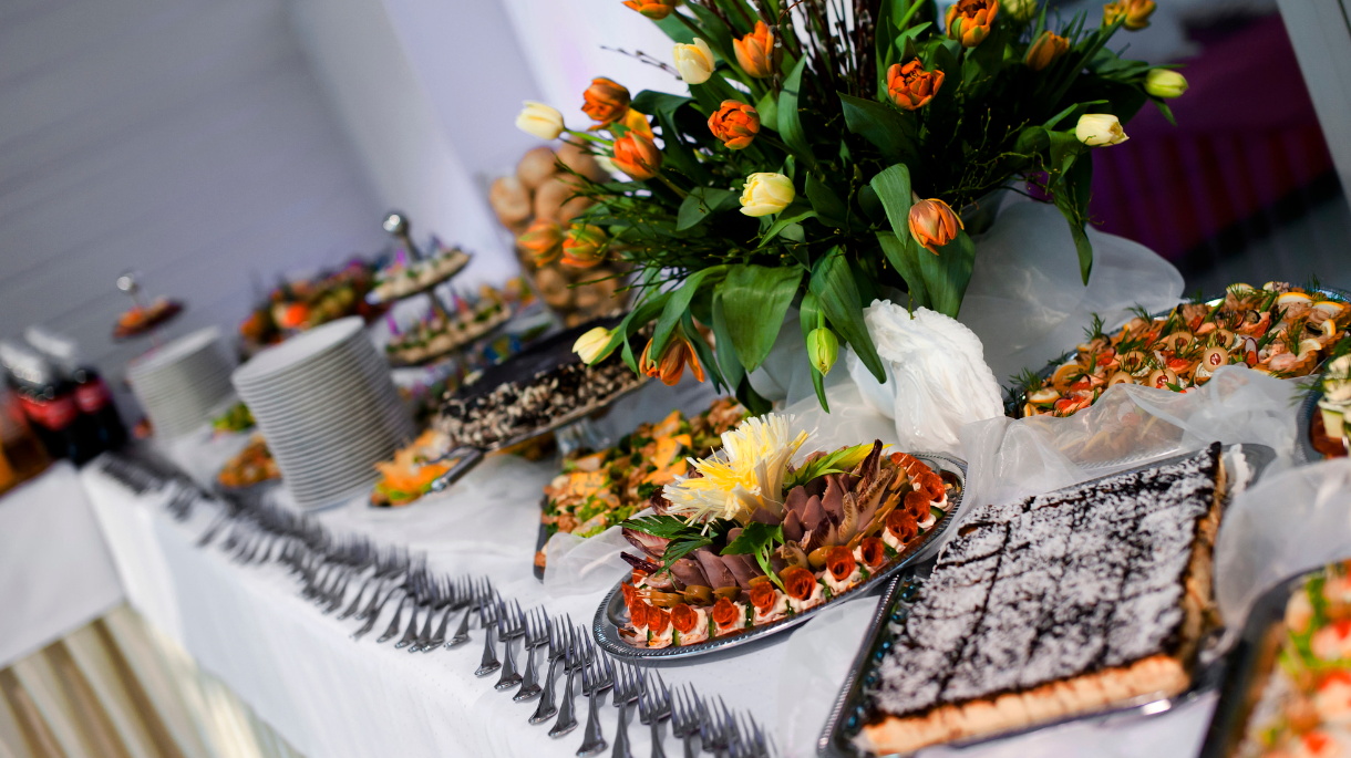 Bufet z różnorodnymi przystawkami i ciastami, ozdobiony bukietem kolorowych tulipanów, idealny na przyjęcia hotelowe