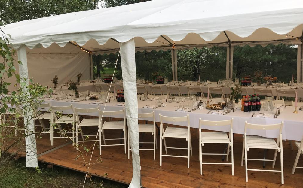 Przyjęcie na zewnątrz pod białym namiotem z długimi stołami udekorowanymi białymi obrusami, kwiatami i napojami.