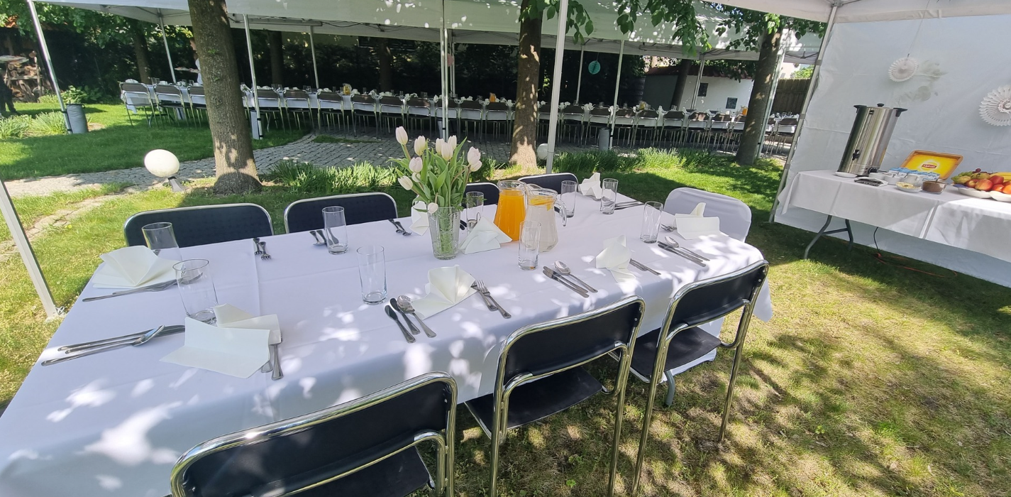 Elegancko nakryty stół na zewnątrz pod namiotem, z bukietem tulipanów i napojami, gotowy na przyjęcie w ogrodzie hotelowym.