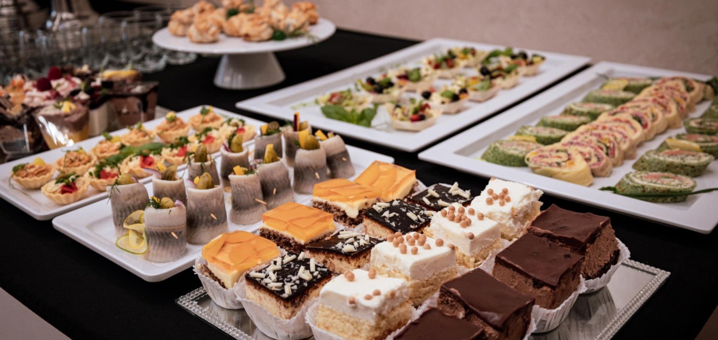 Wykwintne przekąski i desery na eleganckim bufecie, w tym mini tarty, rolady i różnorodne ciasta na czarnym obrusie