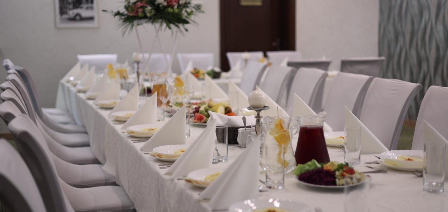 Długi stół nakryty białym obrusem, eleganckie białe serwetki, kwiatowa dekoracja i przystawki gotowe na bankiet lub przyjęcie