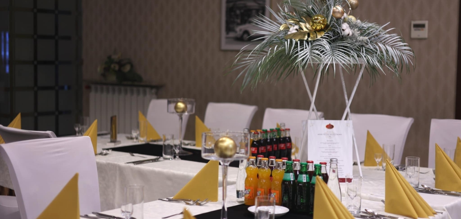 Elegancko nakryty stół bankietowy z białymi obrusami, żółtymi serwetkami i dekoracją z zielonych liści i złotych ozdób