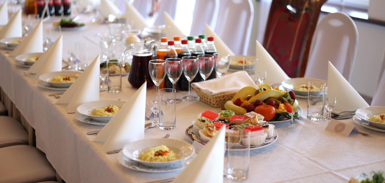Długi, elegancko nakryty stół na bankiet z białymi obrusami, talerzami z makaronem, napojami i deserami