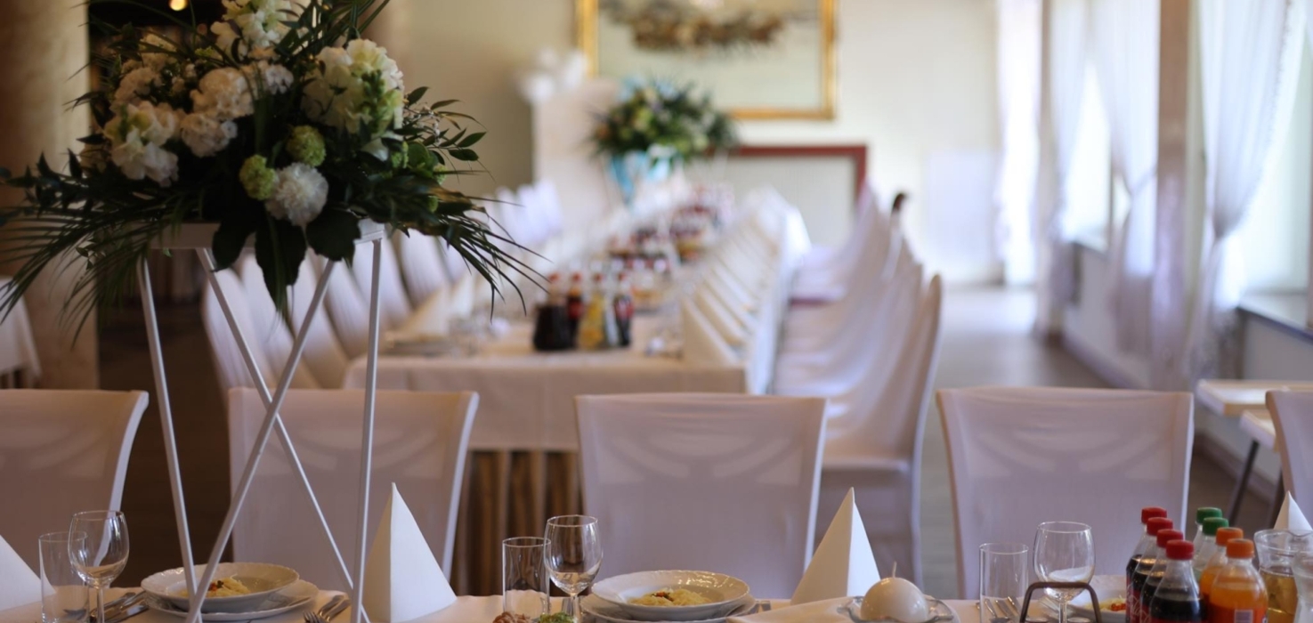 Elegancko udekorowana sala bankietowa z długim stołem, białymi obrusami, bukietami kwiatów i przekąskami na przyjęcie