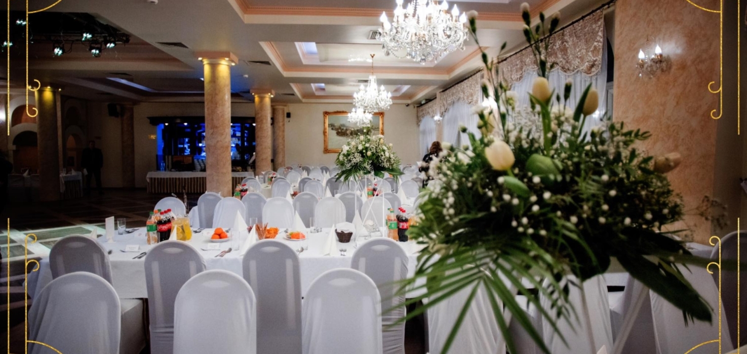 Elegancka sala bankietowa z kryształowymi żyrandolami, udekorowanymi stołami i białymi pokrowcami na krzesła, idealna na wesela