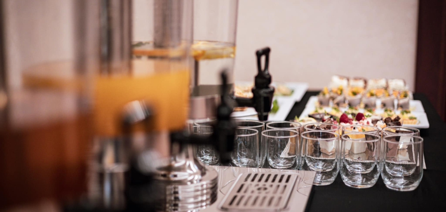 Szklanki ustawione obok dyspenserów z napojami i różnorodnych deserów na stole bufetowym podczas wydarzenia hotelowego