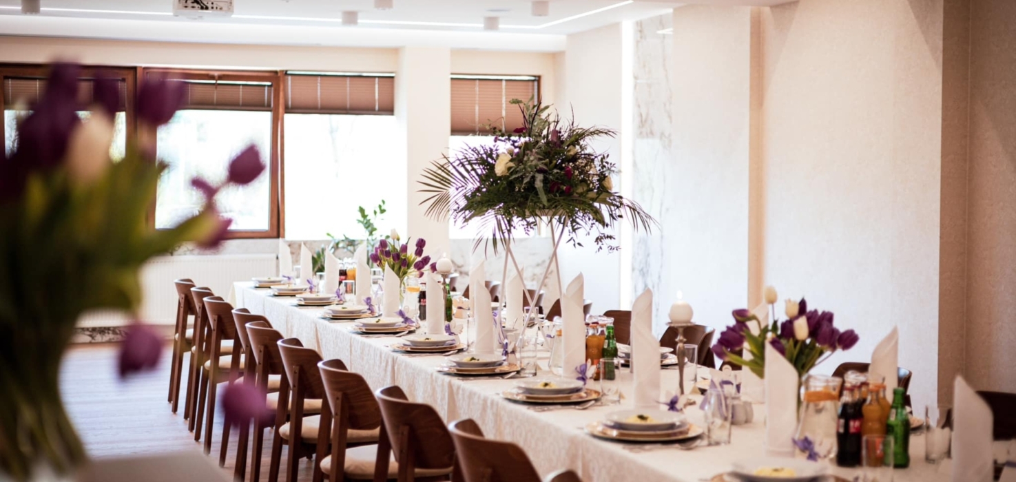 Elegancko nakryty stół bankietowy z dekoracjami kwiatowymi i białymi serwetkami w jasnej sali konferencyjnej hotelu