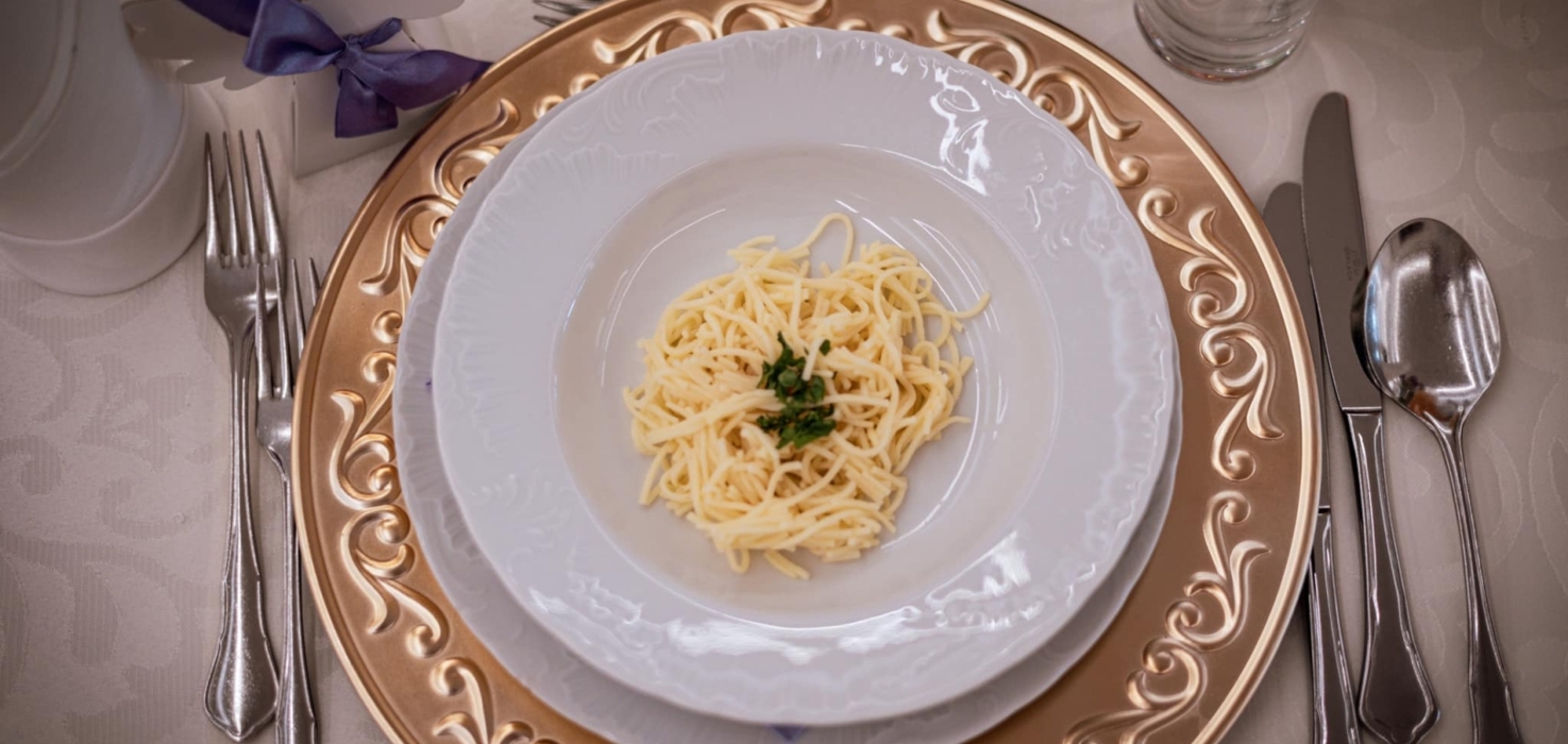 Elegancko podany makaron z pietruszką na białym talerzu z ozdobnym złotym talerzem pod spodem, stół z białym obrusem i sztućcami