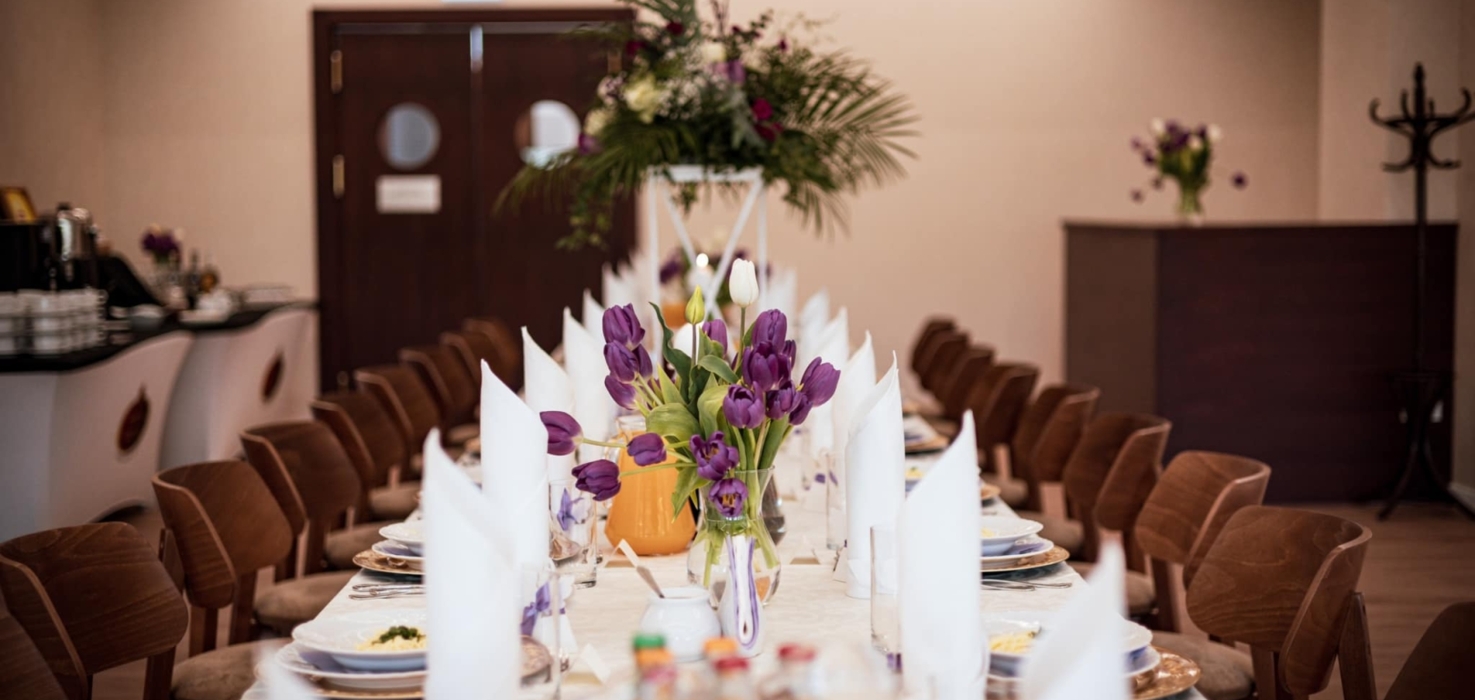 Elegancki, długi stół bankietowy z białymi serwetkami, bukietami fioletowych tulipanów i ustawionymi miejscami dla gości