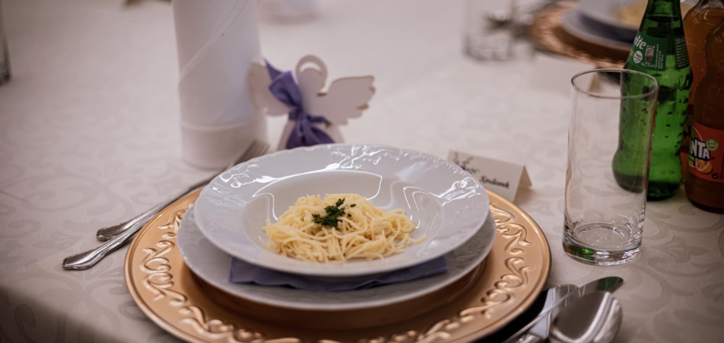 Elegancko nakryty stół z ozdobnym talerzem, makaronem z natką pietruszki i napojami na uroczystą kolację