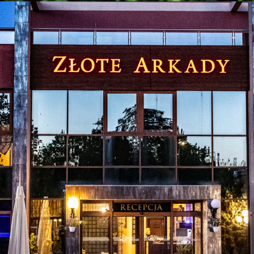 Nowoczesny hotel Złote Arkady z dużymi szklanymi oknami i oświetloną recepcją, w wieczornej atmosferze