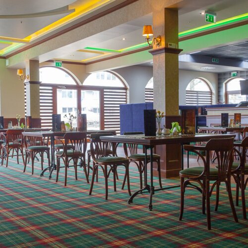 Stylowa restauracja hotelowa z drewnianymi meblami, dużymi arkadowymi oknami i kolorowym, wzorzystym dywanem