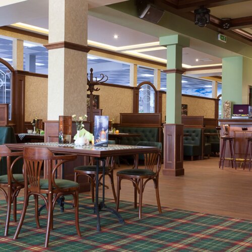 Elegancka restauracja hotelowa z drewnianymi meblami, zielonymi tapicerowanymi kanapami i dobrze zaopatrzonym barem