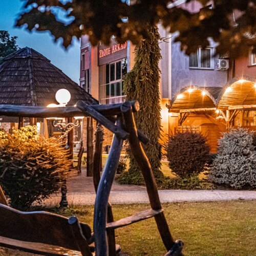 Wieczorny ogród hotelowy z drewnianą altaną, oświetleniem i naturalnymi, rustykalnymi elementami wypoczynkowymi