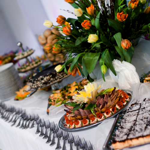 Bufet z różnorodnymi przystawkami i ciastami, ozdobiony bukietem kolorowych tulipanów, idealny na przyjęcia hotelowe