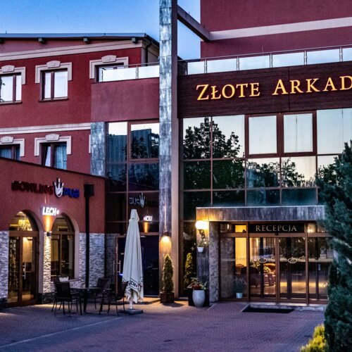 Hotel Złote Arkady z eleganckim wejściem, recepcją, kamiennym wykończeniem i zewnętrznym tarasem z krzesłami przy pubie bowlingowym