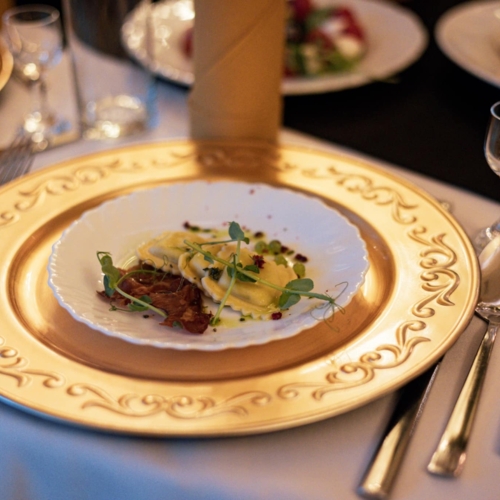 Elegancka przystawka z ravioli i dekoracją z mikroziół na białym talerzu ze złotym wzorem, ustawiona na eleganckim stole